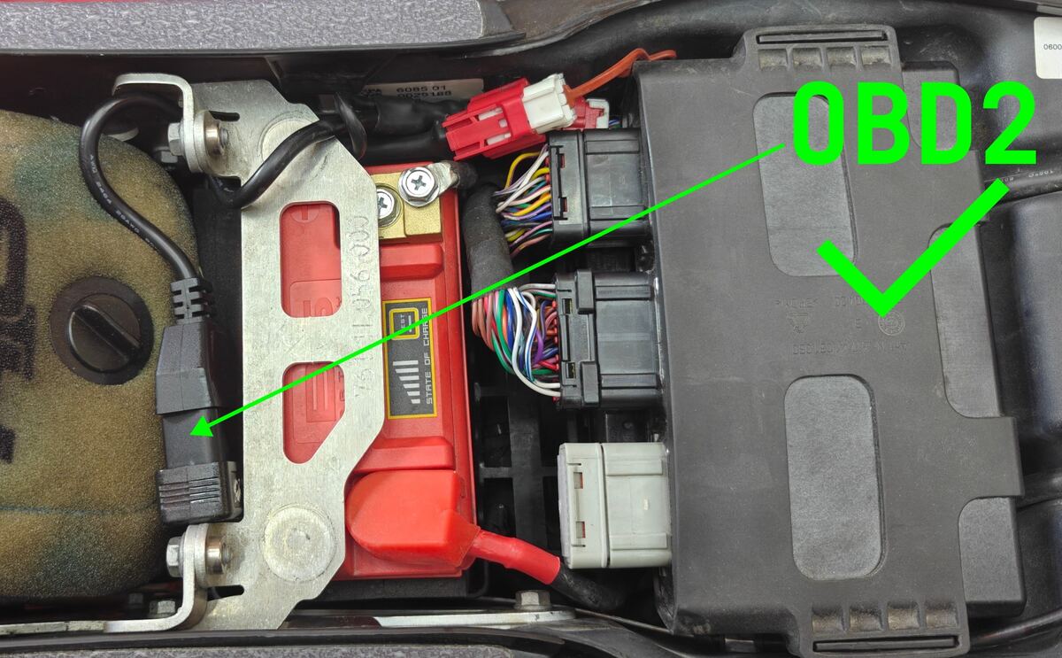 The same space with the dongle moved on top, on the far side of the battery away from the ECU, marked with a green check