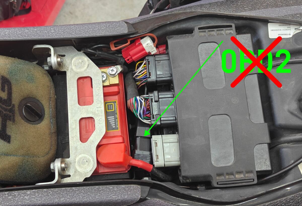Under the seat of a KTM 690, the dongle pushed down into the cavity beside the battery, directly under the ECU, marked with a red cross